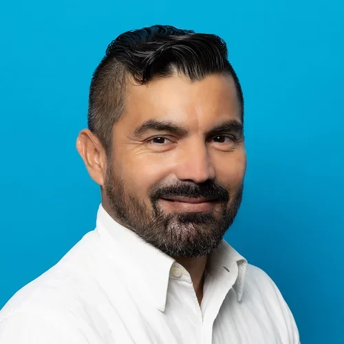 cesar arellano in a white button up shirt on a bright blue background