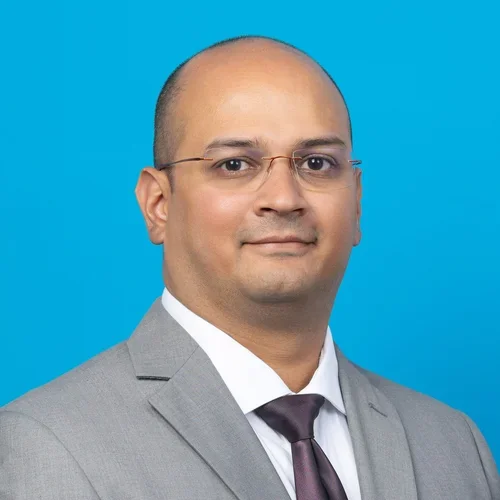 kishore rajendran profile wearing a gray suit and glasses on a light blue background