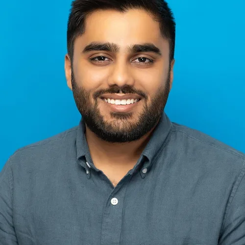 dhruvin shah wearing a charcoal button up shirt on a bright blue background