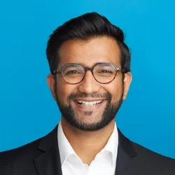varun badheka wearing a black suit on a bright blue background