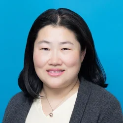 fei ye wearing a charcoal cardigan and white shirt on a bright blue background