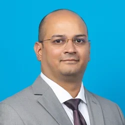 kishore rajendran profile wearing a gray suit and glasses on a light blue background