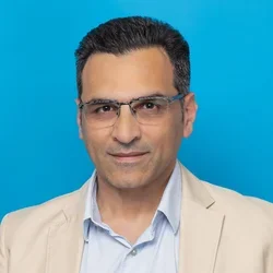 amir shaerzadeh wearing glasses and a cream colored suit on a bright blue background